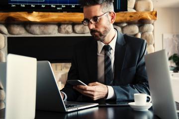 Man in black holding a phone in a coffee shop.