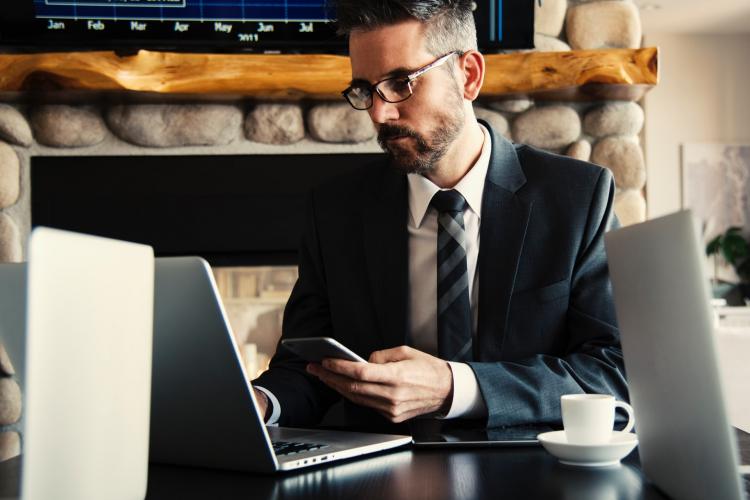 Man in black holding a phone in a coffee shop.